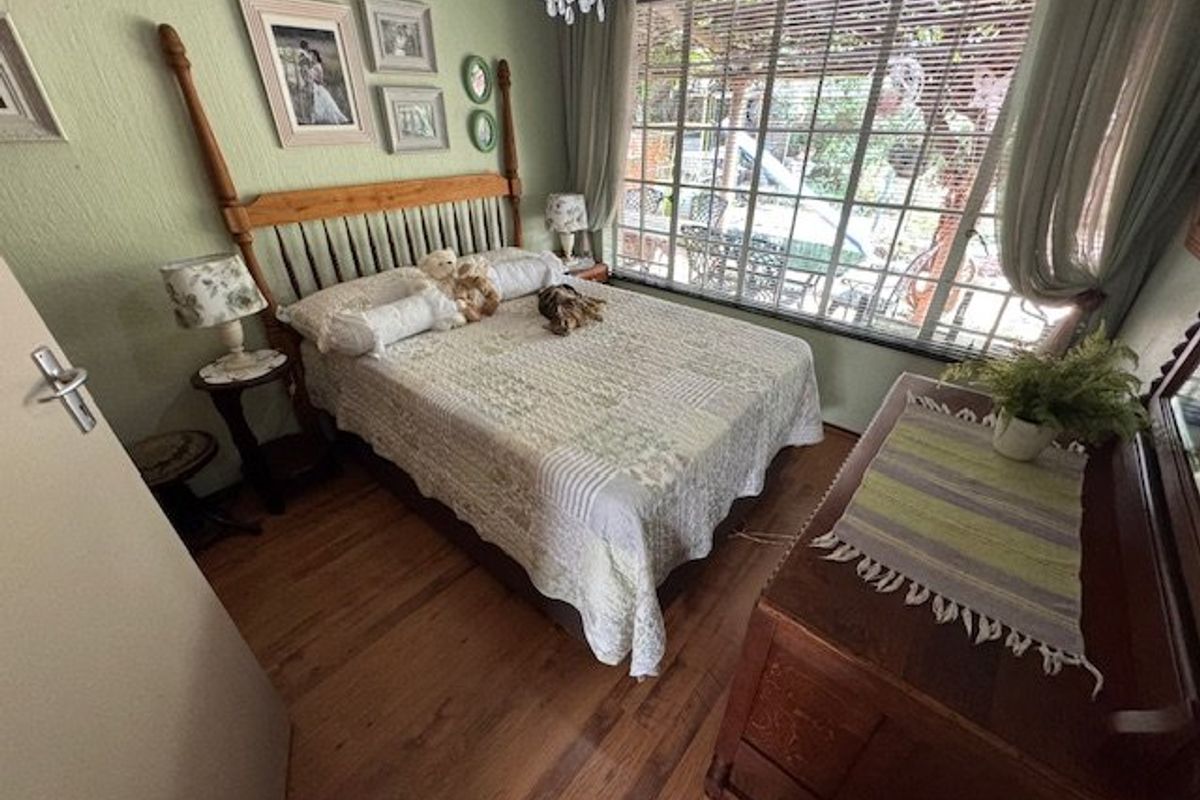 A cozy bedroom featuring hardwood flooring, textured walls, and a large window overlooking the garden, complemented by a decorative crystal chandelier.