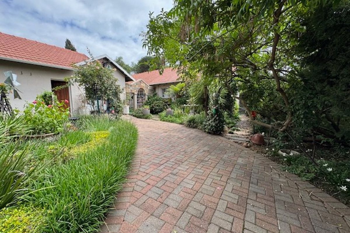 A well-maintained rear exterior view featuring a brick-paved pathway, mature garden landscaping, and a traditional tiled roof house structure.