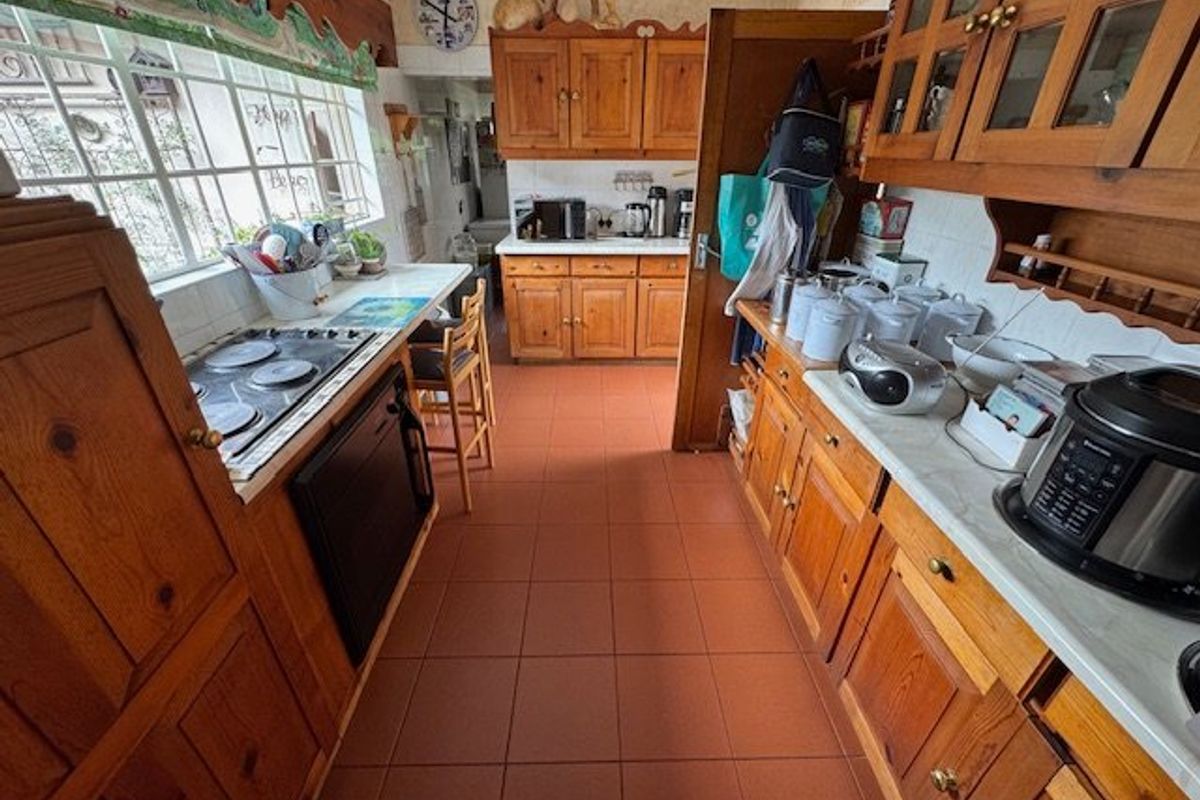 A traditional kitchen featuring extensive wooden cabinetry, tiled flooring, and a built-in hob, offering a functional layout with classic design elements.