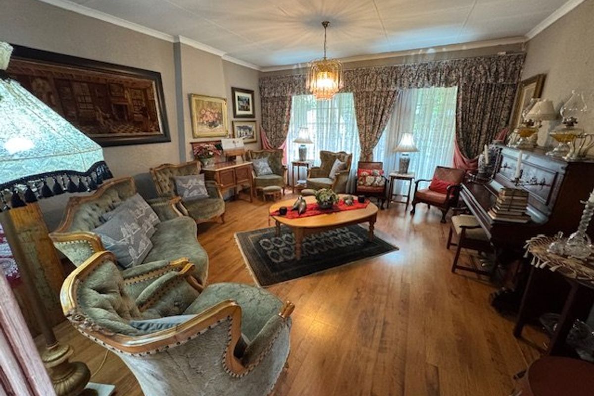 A traditional living room featuring hardwood flooring, decorative ceiling cornice, and a central chandelier, offering a classic and well-maintained living space.
