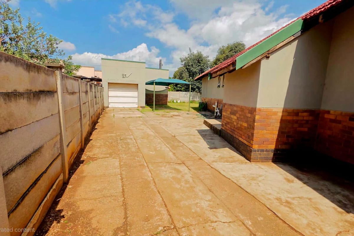 Rear exterior view showing a concrete driveway, brick and plaster house facade, and a detached garage with a precast concrete boundary wall.