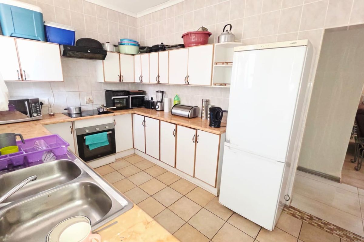 A functional kitchen featuring white cabinetry, laminate countertops, a double stainless steel sink, and built-in cooking appliances with tiled walls and flooring.