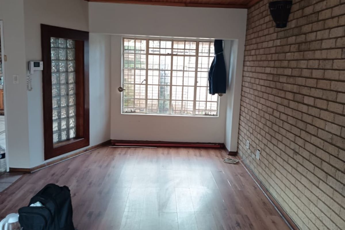 An empty living room featuring a timber-clad ceiling, exposed brick feature wall, and laminate flooring with security-barred windows.