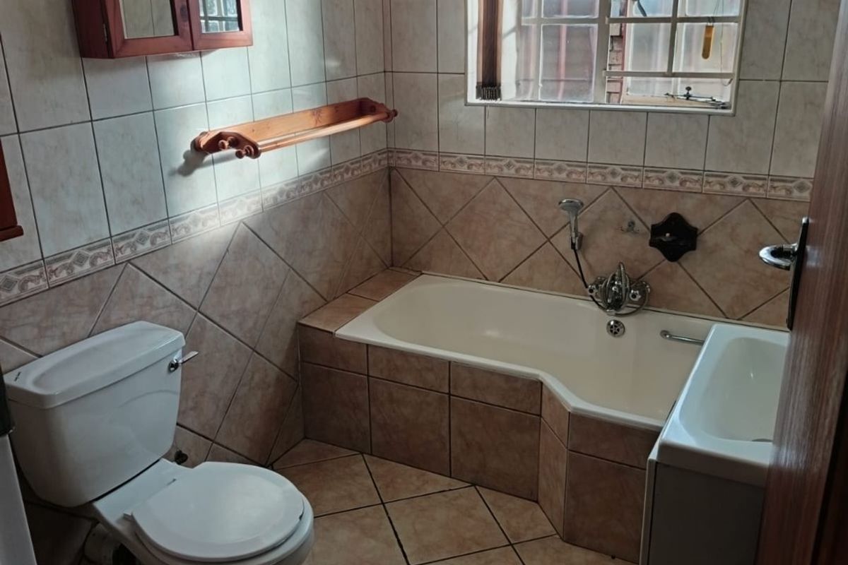 A functional bathroom featuring a built-in bathtub, toilet, and vanity basin with neutral wall and floor tiling.