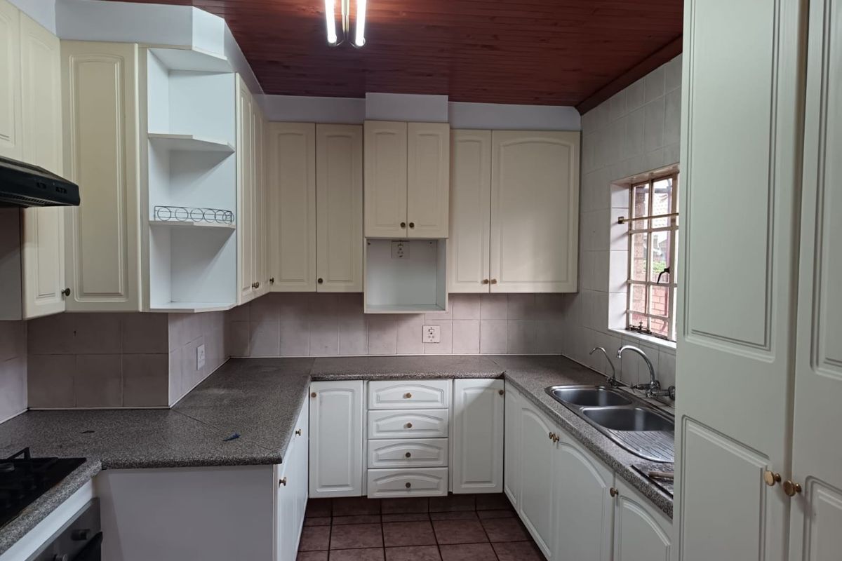 A functional kitchen featuring built-in cabinetry, laminate countertops, a double stainless steel sink, and a timber ceiling, offering a dated but well-maintained layout.