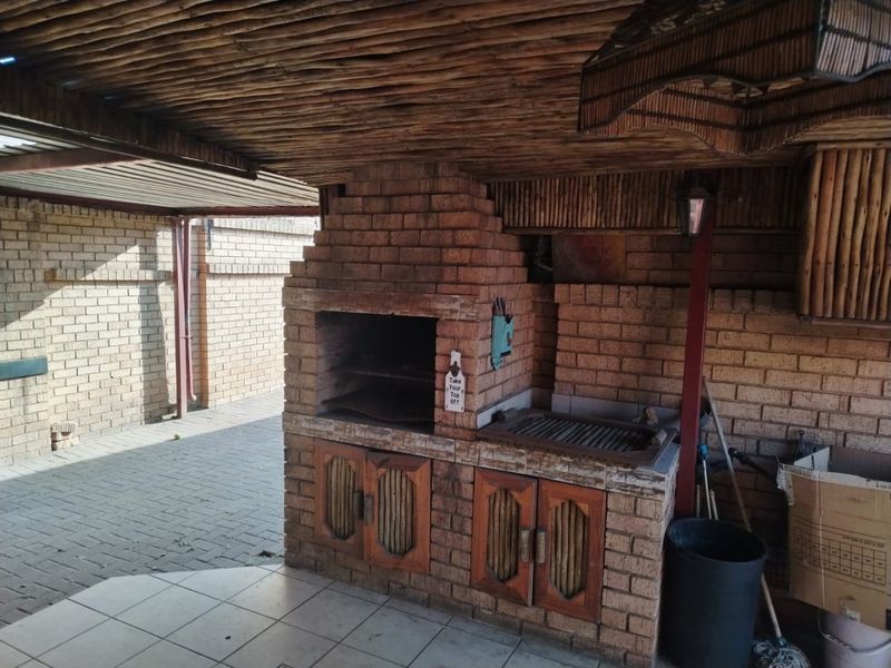 Covered outdoor patio area featuring a substantial built-in brick braai, thatched roofing, and paved flooring, ideal for outdoor entertaining.