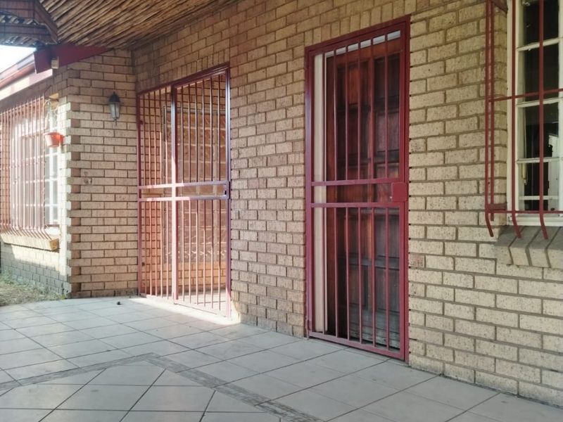 A covered patio area featuring face brick walls, tiled flooring, and a rustic timber beam ceiling, secured with metal gates and window bars.