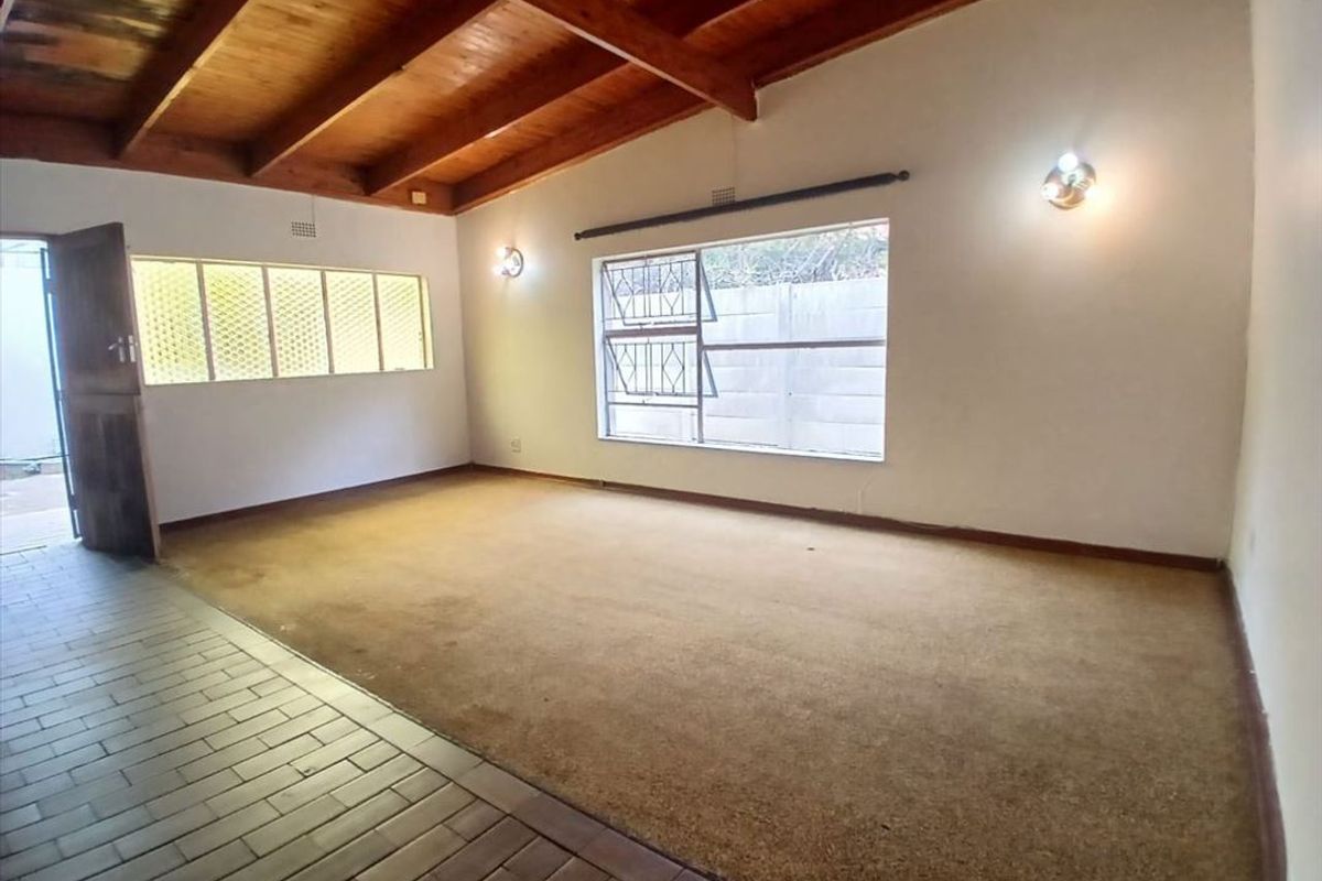 Spacious living area featuring exposed timber beam ceilings, a combination of tiled and carpeted flooring, and large windows with security bars.