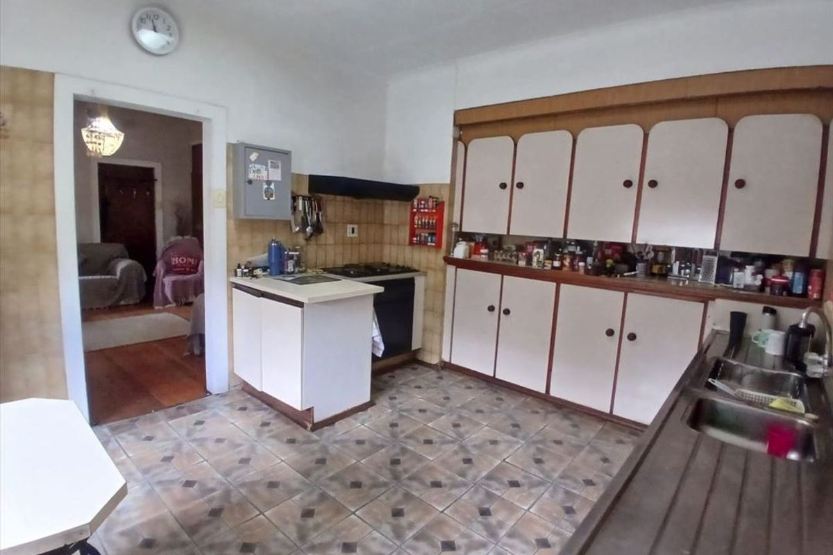 A dated kitchen featuring original cabinetry, a gas hob with extractor, and a double bowl stainless steel sink with tiled splashbacks.