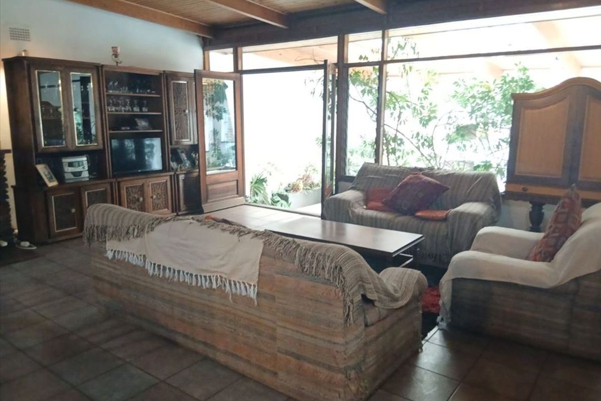 Spacious living room featuring exposed timber beam ceilings, tiled flooring, and large glass sliding doors providing natural light and access to the outdoor area.