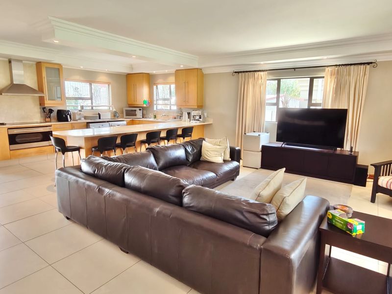 Spacious open-plan living area featuring a modern kitchen with built-in cabinetry, a breakfast island, and tiled flooring throughout, seamlessly connecting to the lounge.