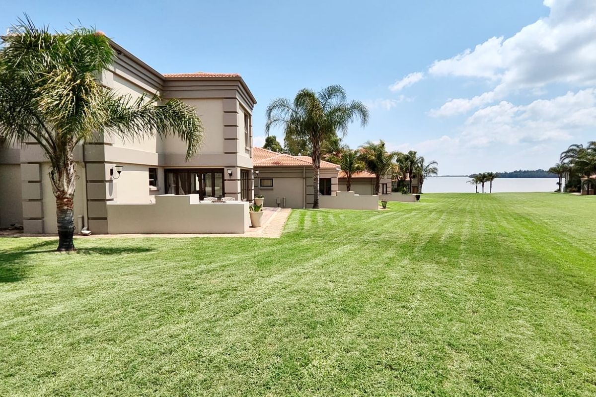 A well-maintained rear exterior view of the property featuring a spacious lawn, paved patio areas, and direct access to the waterfront.