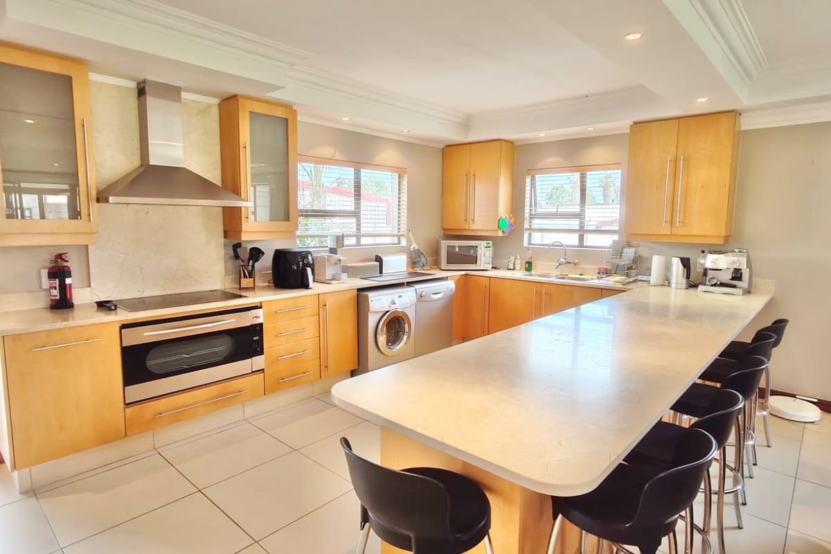 Spacious kitchen featuring light wood cabinetry, stone countertops, a large central island, and integrated stainless steel appliances, offering a functional and bright cooking space.