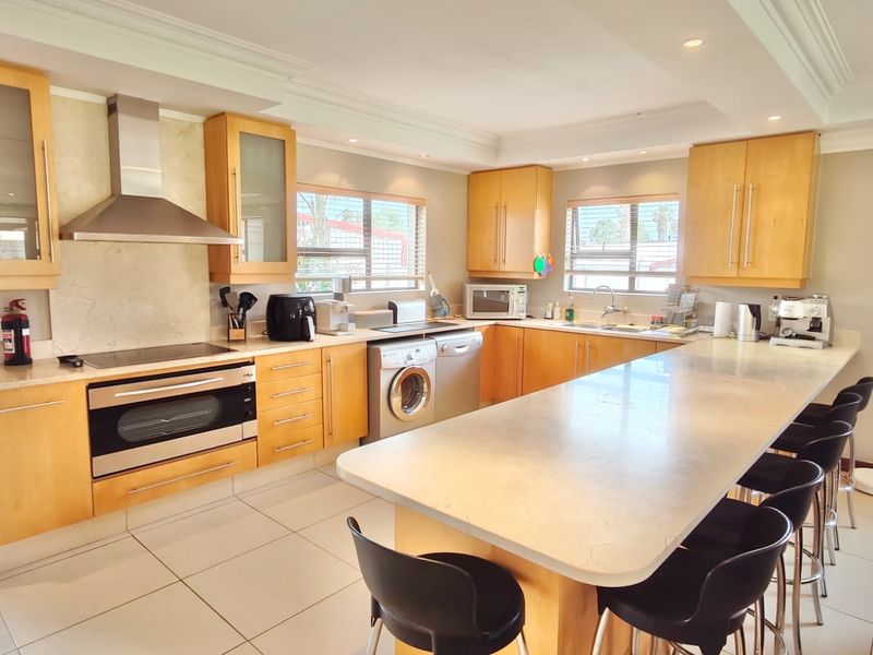 Spacious kitchen featuring light wood cabinetry, stone countertops, a large central island, and integrated stainless steel appliances, offering a functional and bright cooking space.