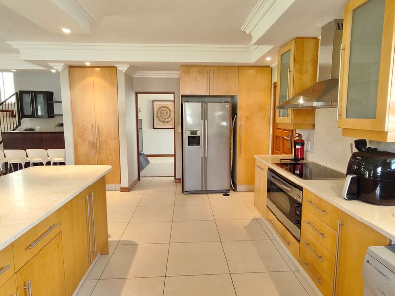 Spacious kitchen featuring light wood cabinetry, stone countertops, a central island, and integrated stainless steel appliances, seamlessly flowing into the open-plan living area.