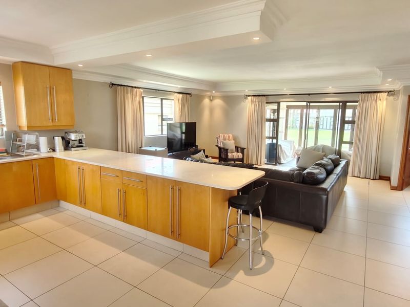 Spacious open-plan living area featuring a modern kitchen with stone countertops, wooden cabinetry, and seamless flow to the outdoor patio through sliding glass doors.
