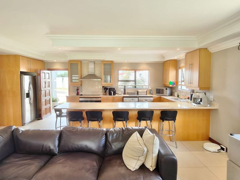Spacious open-plan kitchen and living area featuring light wood cabinetry, a large breakfast island with stone countertops, and integrated appliances.