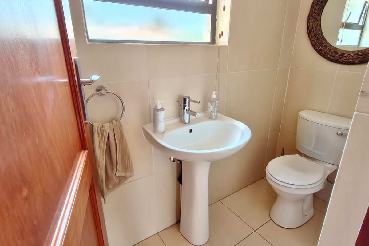 A compact, well-maintained bathroom featuring a pedestal basin with a chrome mixer tap, a standard toilet, and neutral wall and floor tiling.