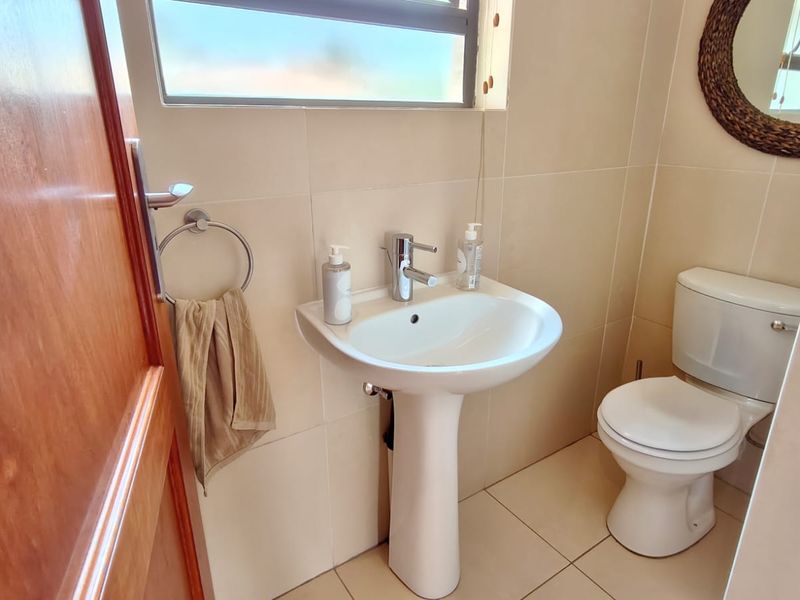 A compact, well-maintained bathroom featuring a pedestal basin with a chrome mixer tap, a standard toilet, and neutral wall and floor tiling.