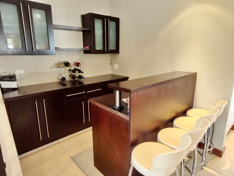 A dedicated home bar area featuring dark wood built-in cabinetry, a matching bar counter, and tiled flooring.
