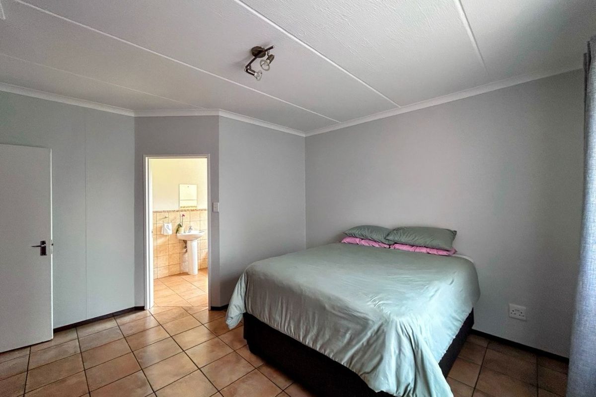 A bedroom featuring tiled flooring and an en-suite bathroom, providing a functional and neutral living space.