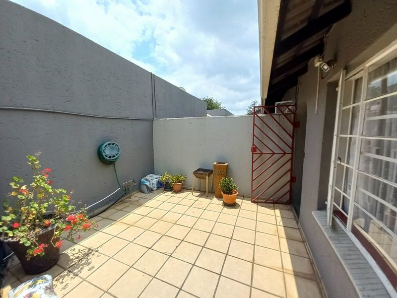 A private paved patio area featuring high boundary walls, a security gate, and direct access to the townhouse interior.