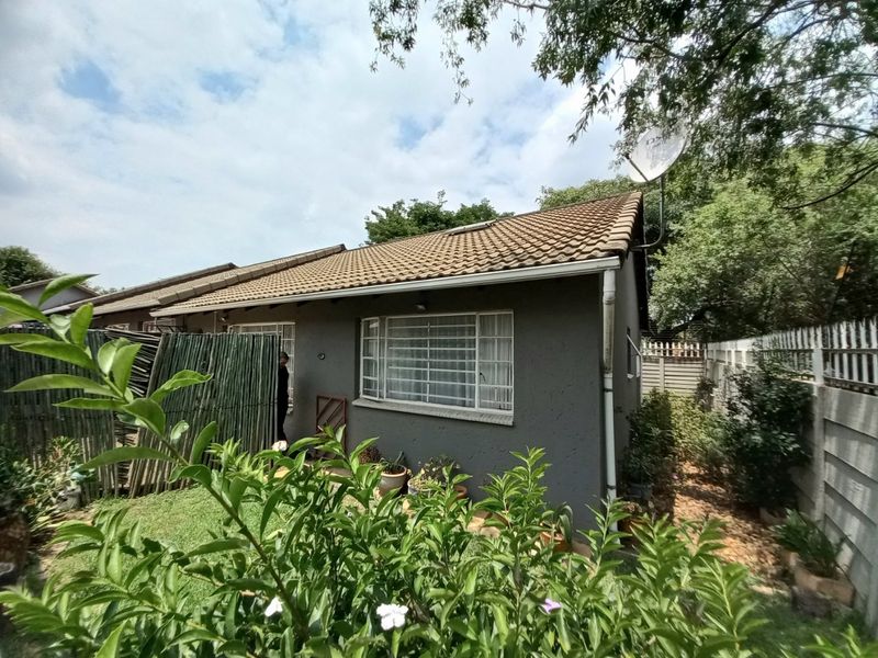A rear view of the townhouse featuring a tiled roof, security-barred windows, and a private garden area with perimeter walling.