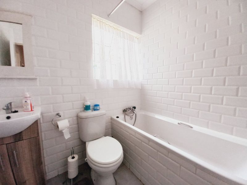 A compact bathroom featuring white subway wall tiles, a built-in bathtub with shower mixer, a pedestal vanity, and a standard toilet.