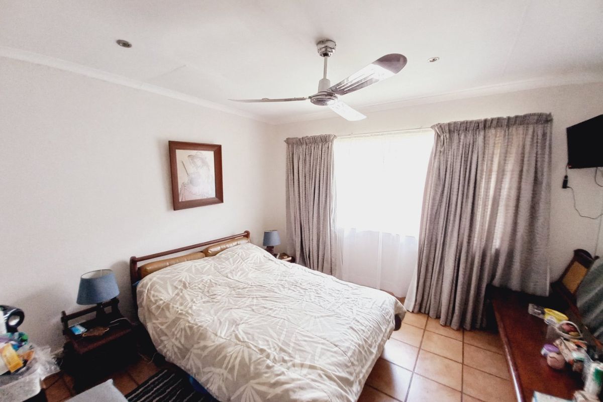 A bedroom featuring tiled flooring, a ceiling fan, and large windows with curtains, providing a functional and comfortable living space.