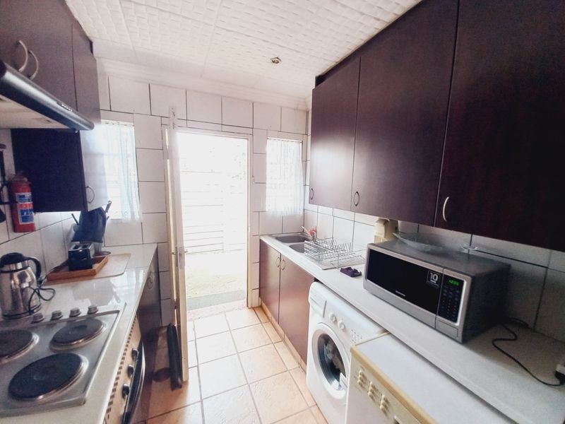 A functional galley-style kitchen featuring dark cabinetry, tiled splashbacks, built-in hob, and direct access to an outdoor area.