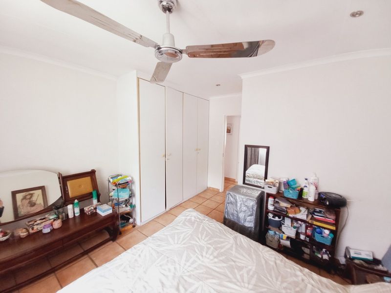 A bedroom featuring built-in cupboards, tiled flooring, and a ceiling fan, offering a functional space with neutral finishes.