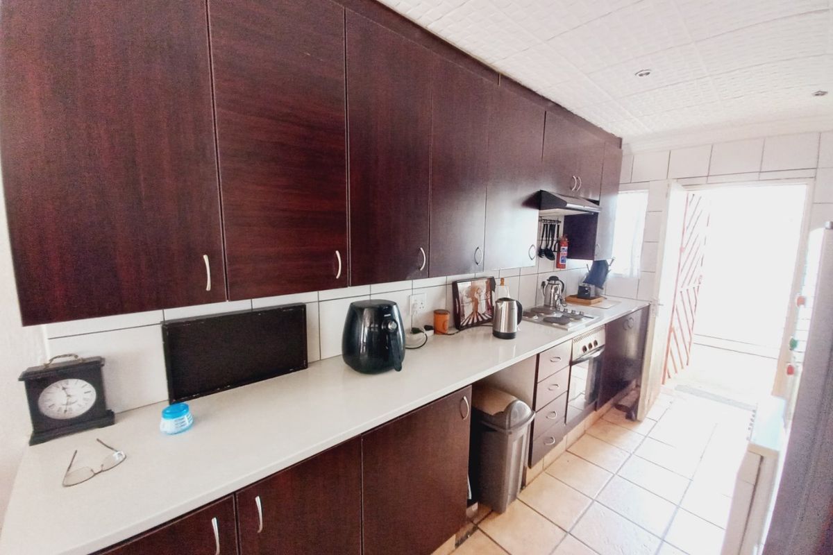 A functional kitchen featuring dark wood-finish cabinetry, white countertops, tiled flooring, and a built-in oven with an extractor fan.