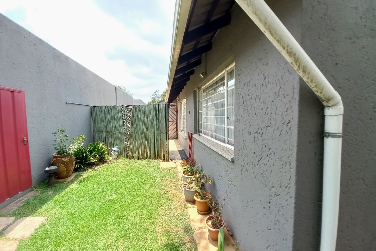 A side garden area featuring a lawn, textured exterior wall, and security bars on the windows, providing a private outdoor space.
