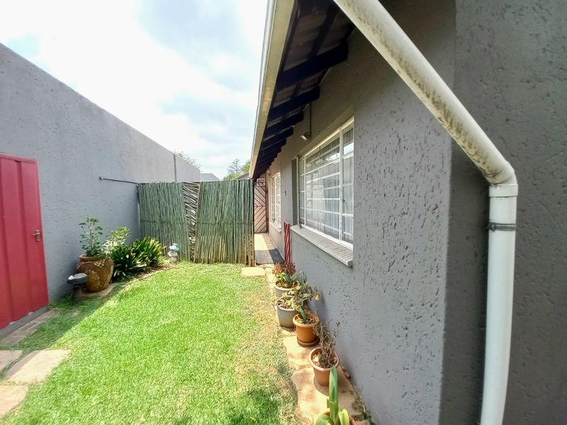 A side garden area featuring a lawn, textured exterior wall, and security bars on the windows, providing a private outdoor space.
