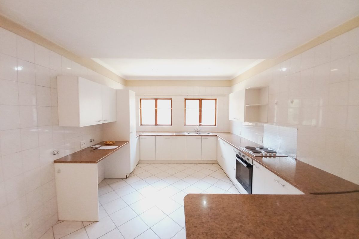 A spacious, empty kitchen featuring white cabinetry, granite countertops, tiled flooring, and built-in cooking appliances, offering a clean canvas for potential updates.