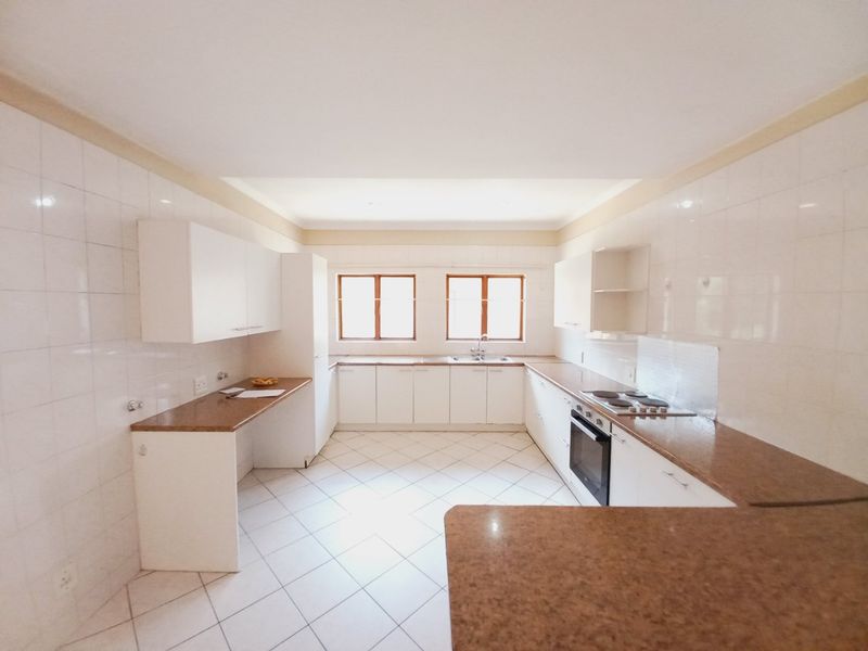 A spacious, empty kitchen featuring white cabinetry, granite countertops, tiled flooring, and built-in cooking appliances, offering a clean canvas for potential updates.