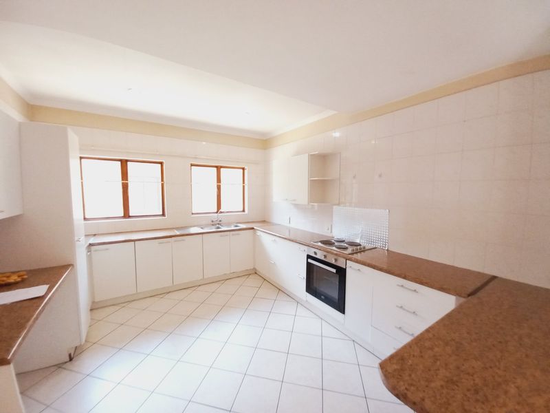 A spacious, empty kitchen featuring white built-in cabinetry, laminate countertops, tiled flooring, and integrated oven and hob.