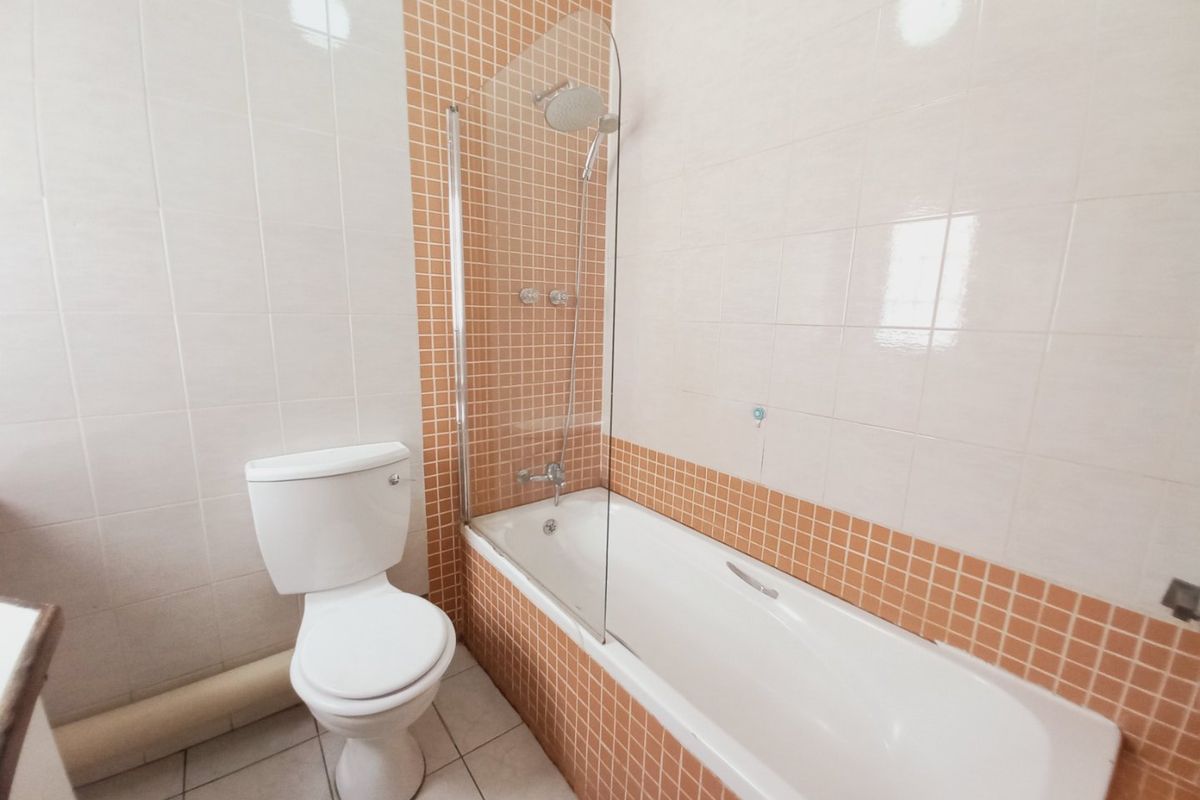 A functional bathroom featuring a bathtub with a glass shower screen, a toilet, and classic tiled finishes throughout.