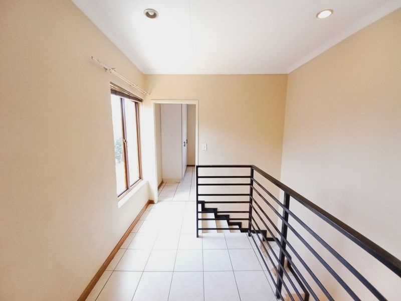 A bright, tiled hallway featuring a modern metal staircase railing, recessed lighting, and access to an adjacent room with built-in storage.