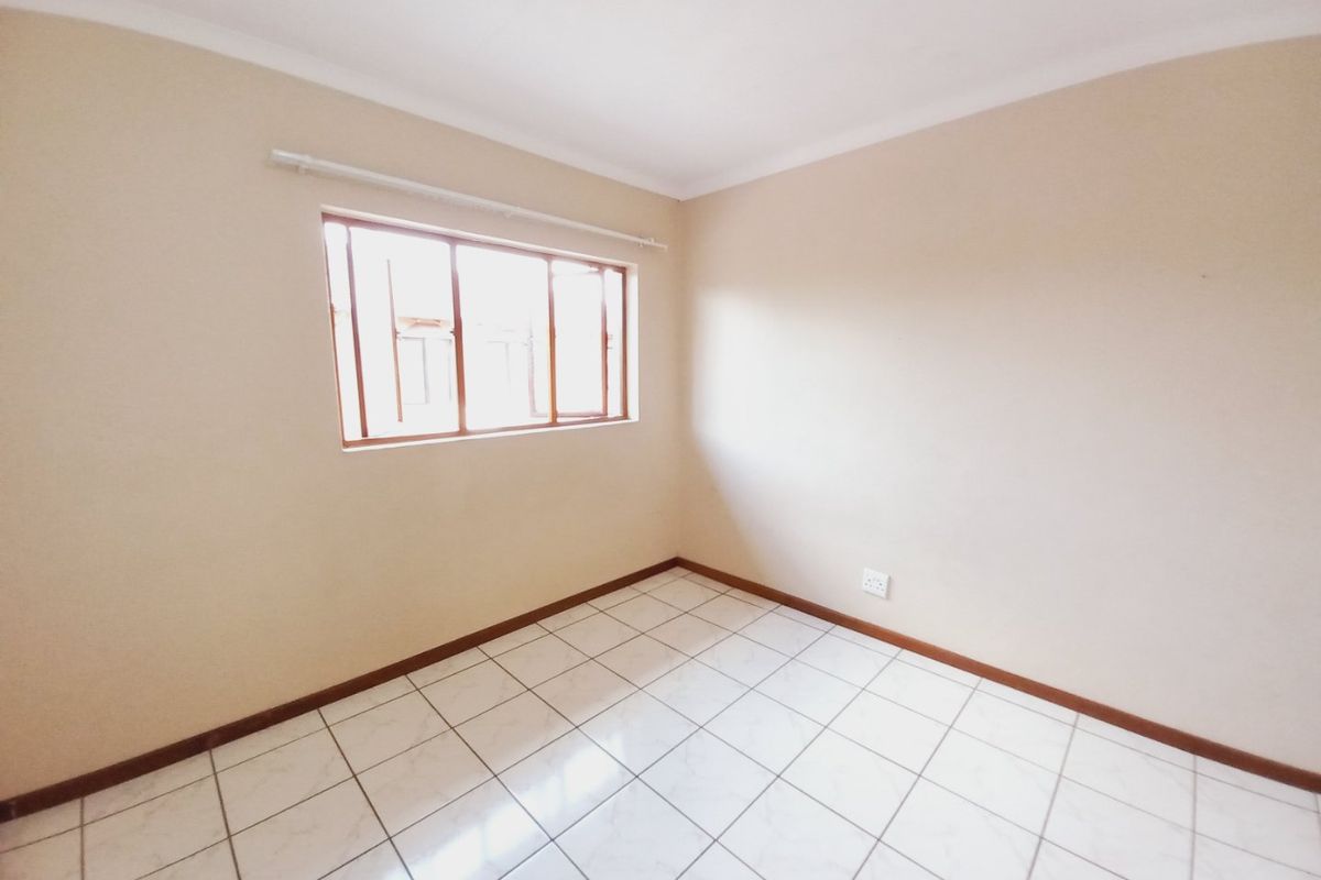 A bright, empty bedroom featuring tiled flooring, neutral walls, and a window with a wooden frame.