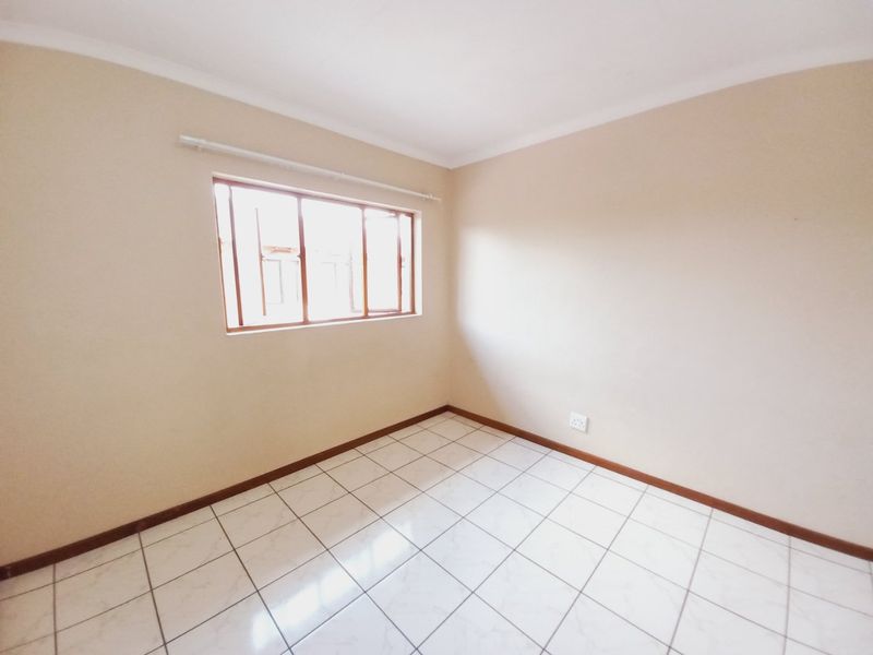 A bright, empty bedroom featuring tiled flooring, neutral walls, and a window with a wooden frame.