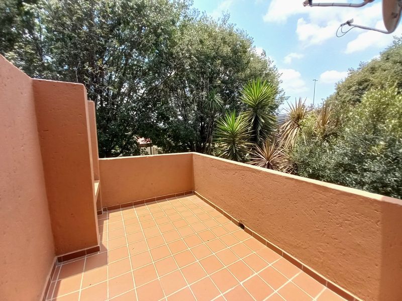 An open-air balcony featuring terracotta-style tiled flooring and a built-in masonry bench, offering a private outdoor space with surrounding greenery.