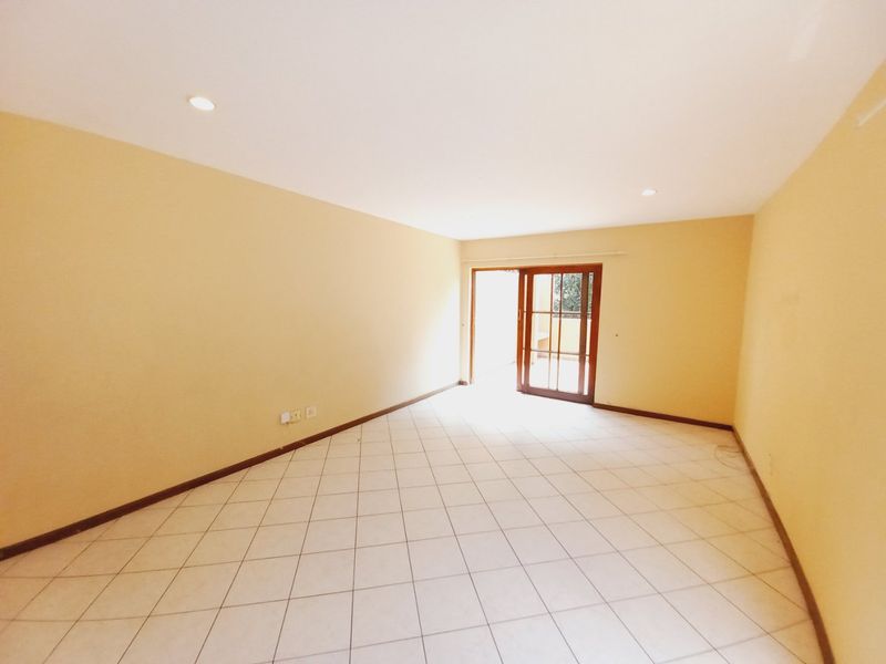 A spacious, empty living area featuring neutral walls, tiled flooring, recessed lighting, and a sliding glass door providing access to the outdoors.