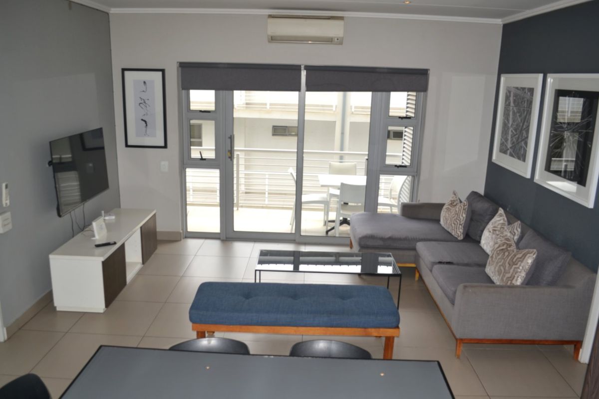 A well-maintained living room featuring tiled floors, recessed lighting, and large sliding glass doors that provide access to an attached balcony.