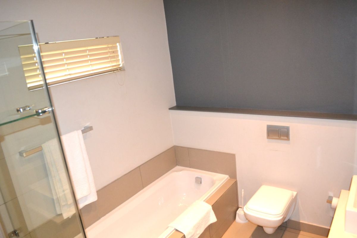 Modern bathroom featuring a built-in bathtub, wall-mounted toilet with concealed cistern, and a glass shower screen.