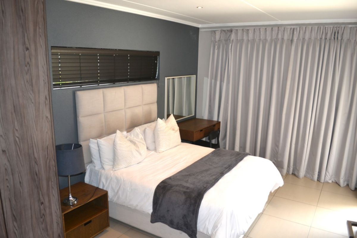 A well-maintained bedroom featuring tiled flooring, built-in wardrobe storage, and neutral window treatments including venetian blinds and full-length curtains.