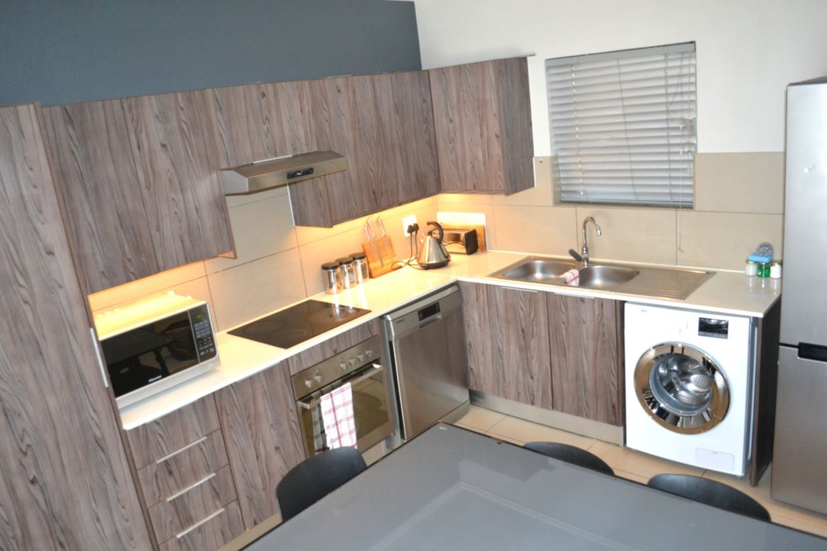 Modern kitchen featuring wood-grain laminate cabinetry, stone countertops, integrated appliances, and a tiled splashback with under-cabinet lighting.