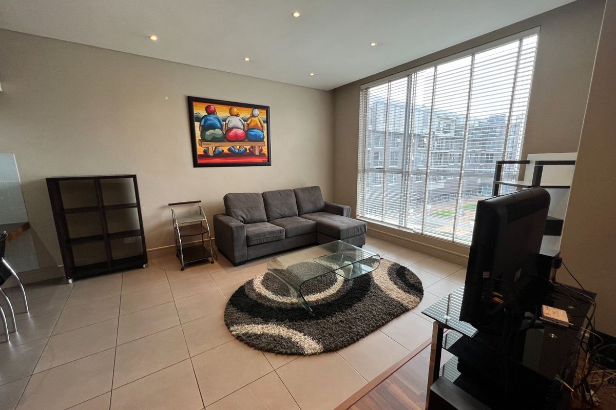 A well-lit living room featuring large floor-to-ceiling windows with venetian blinds and neutral ceramic floor tiles.