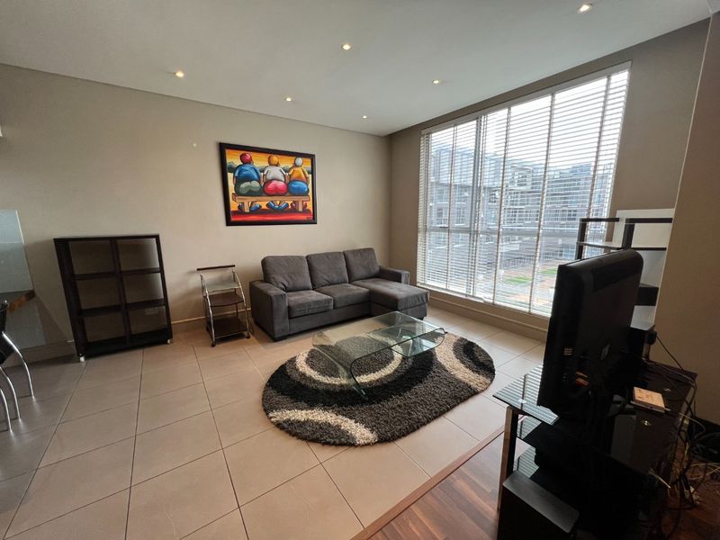 A well-lit living room featuring large floor-to-ceiling windows with venetian blinds and neutral ceramic floor tiles.