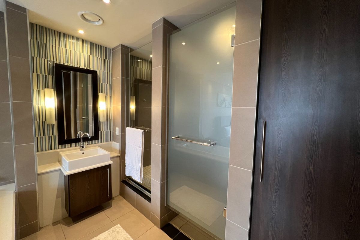 Modern bathroom featuring a vessel sink vanity, walk-in shower with frosted glass door, and contemporary tiled finishes with integrated lighting.